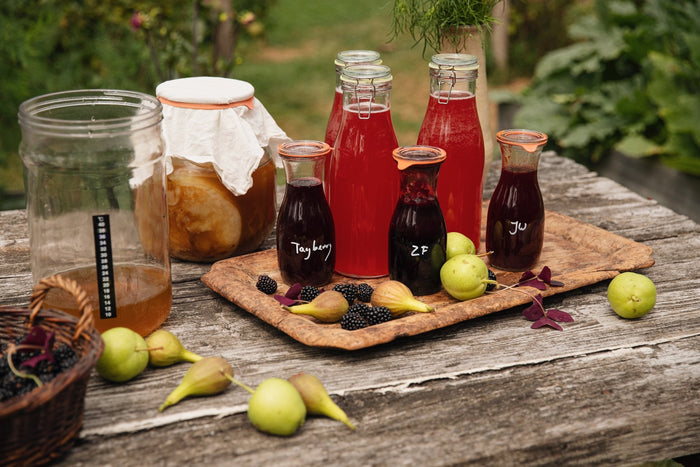 Beugelflessen kombucha en fermentatiepotten op een tuintafel