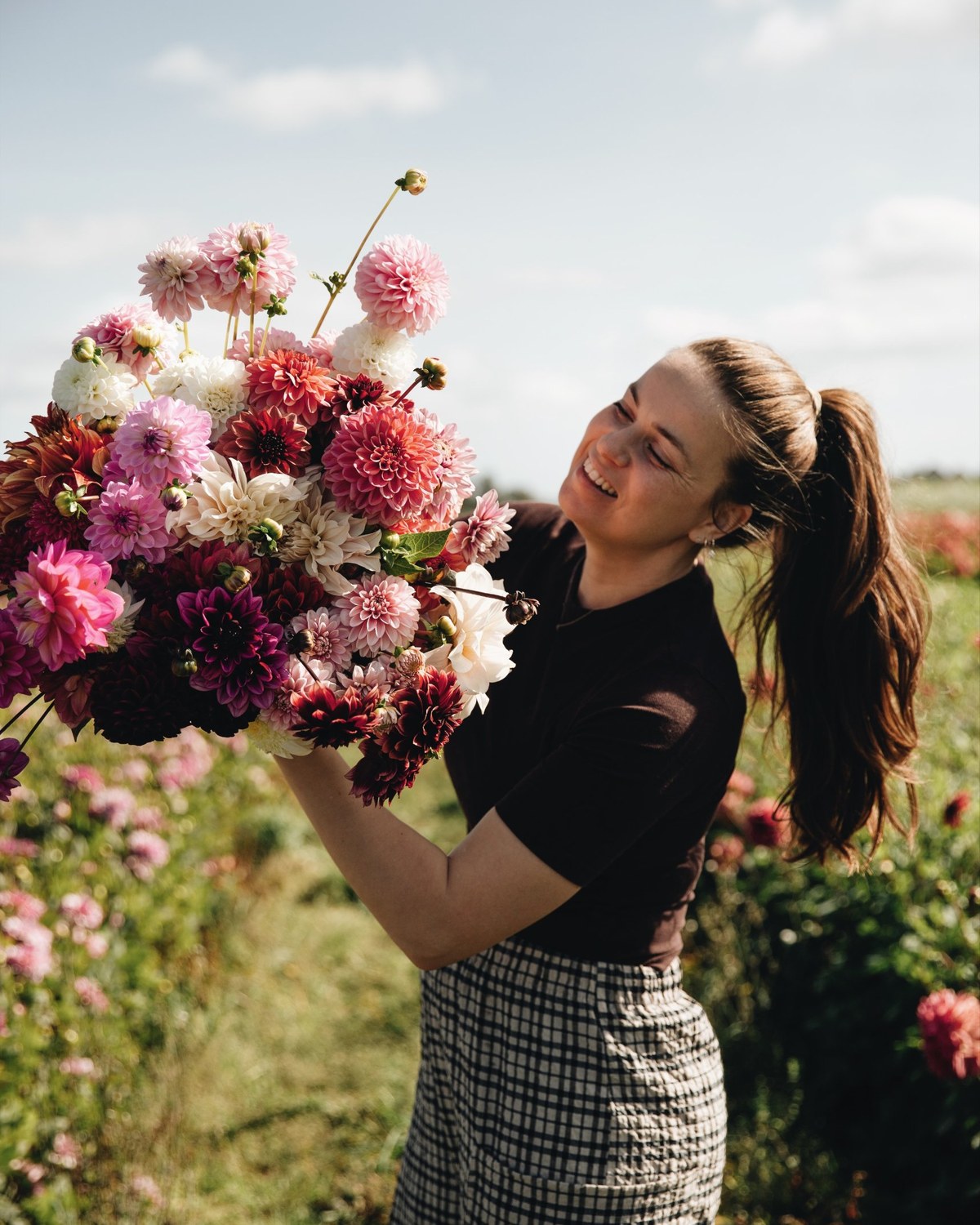 Merel lacht met een groot boeket van haar favoriete dahlia's in het veld: dahliapakket Merels favorieten van De Groene Makers